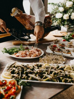 A chef slices meat in a beautifully arranged catering setup with diverse appetizing dishes.