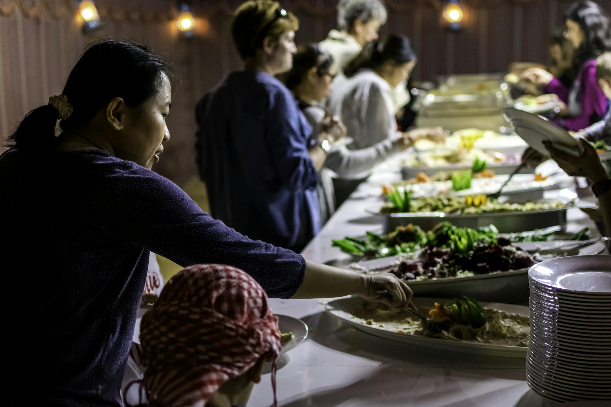 A diverse group of people enjoying a buffet dinner indoors with various dishes.